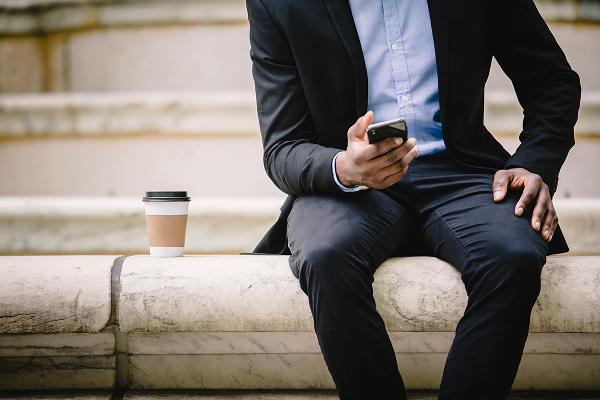 Crop businessman using smartphone while resting on bench with takeaway coffee